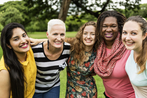 Group of diverse women smiling together in a park, representing community support and connection in group therapy settings.