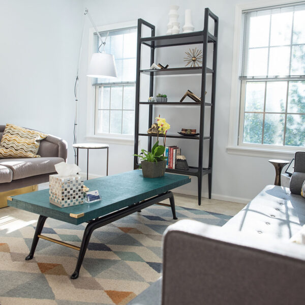 Cozy therapy office with a green coffee table, gray sofas, decorative shelves, and natural light, reflecting a welcoming environment for marriage counseling and psychotherapy sessions.