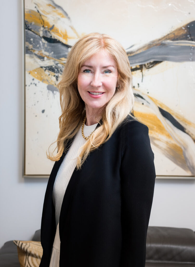 Professional therapist smiling in a black blazer against an abstract art background, representing mental health services for individuals and families.