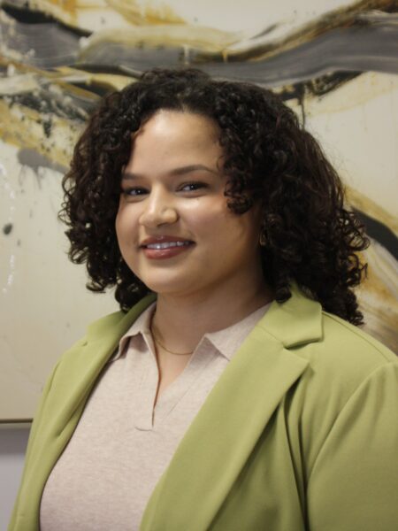 Estefani Betancourt, LAC, smiling in a professional green blazer, in front of an abstract background, representing a therapist at Dr. Stephen Oreski & Associates.