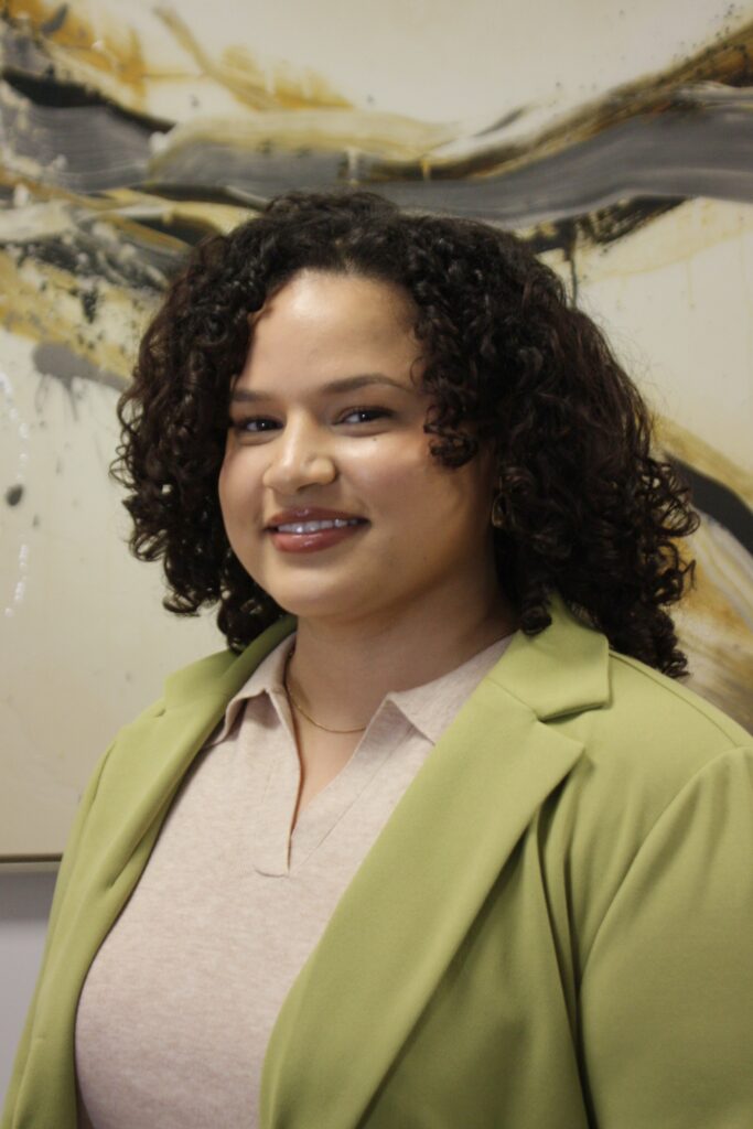 Smiling female therapist in a green blazer, posing in front of abstract art, representing child and teen therapy services at Dr. Stephen Oreski & Associates.