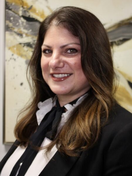 Professional therapist smiling, wearing a black blazer with a white blouse and black tie, set against an abstract background, representing Dr. Stephen Oreski & Associates psychotherapy practice.