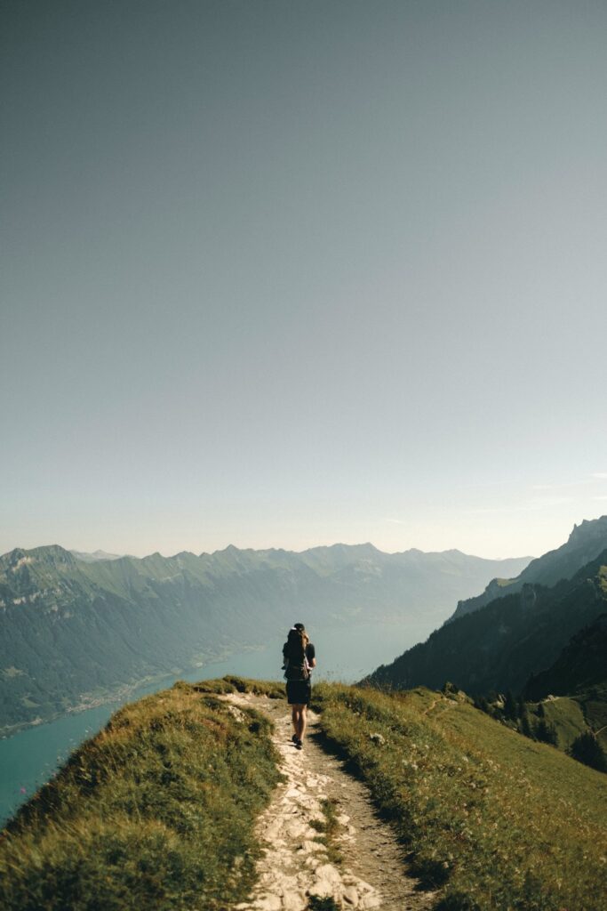 Person hiking on a scenic mountain path overlooking a lake and valley, representing themes of nature and mental health benefits of outdoor activities.