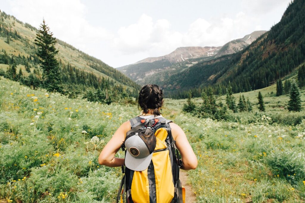 Hiker with a yellow backpack walking through a lush green valley surrounded by mountains, reflecting themes of exploration and emotional healing related to toxic relationships.