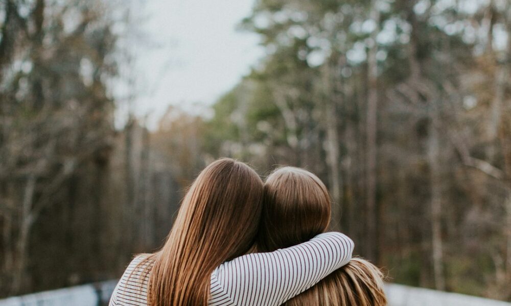 Two women embracing in a supportive hug, standing together in a serene forest setting, symbolizing emotional support for loved ones with bipolar disorder.