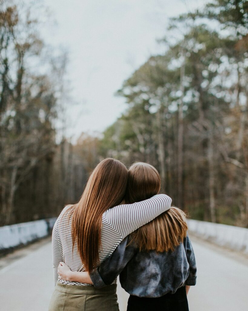 Two women embracing on a quiet road, symbolizing support and connection in mental health, relevant to therapy and coping with challenges like bipolar disorder.