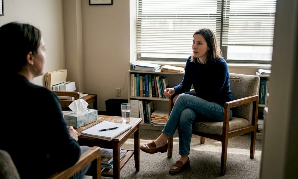 Psychotherapist and client engaged in an in-person therapy session in an urban office, discussing emotional wellbeing and coping strategies.