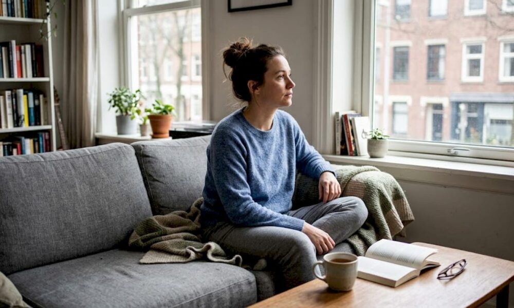Mujer sentada en el sof&aacute; de su sal&oacute;n, absorta en sus pensamientos.