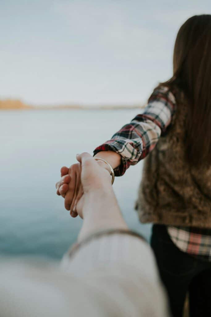 Couple holding hands by the water, symbolizing connection and relationship support, relevant to couples and marriage therapy themes.