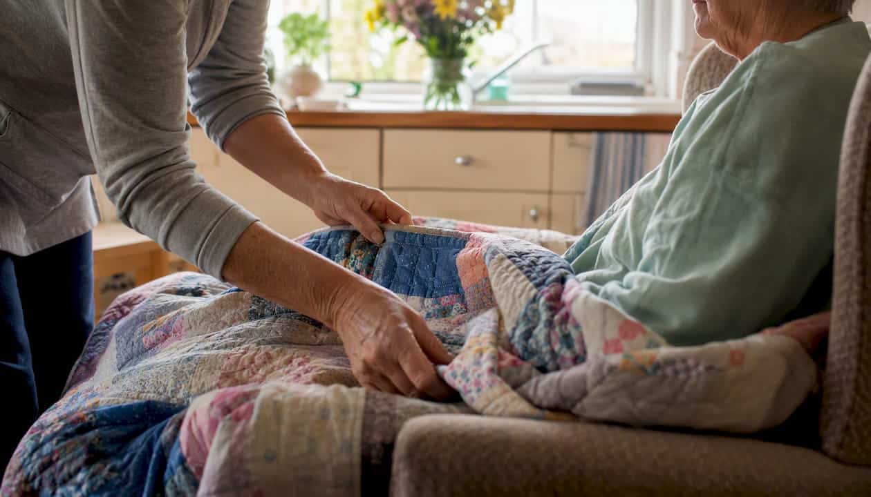 Caregiver adjusting blanket for elderly person